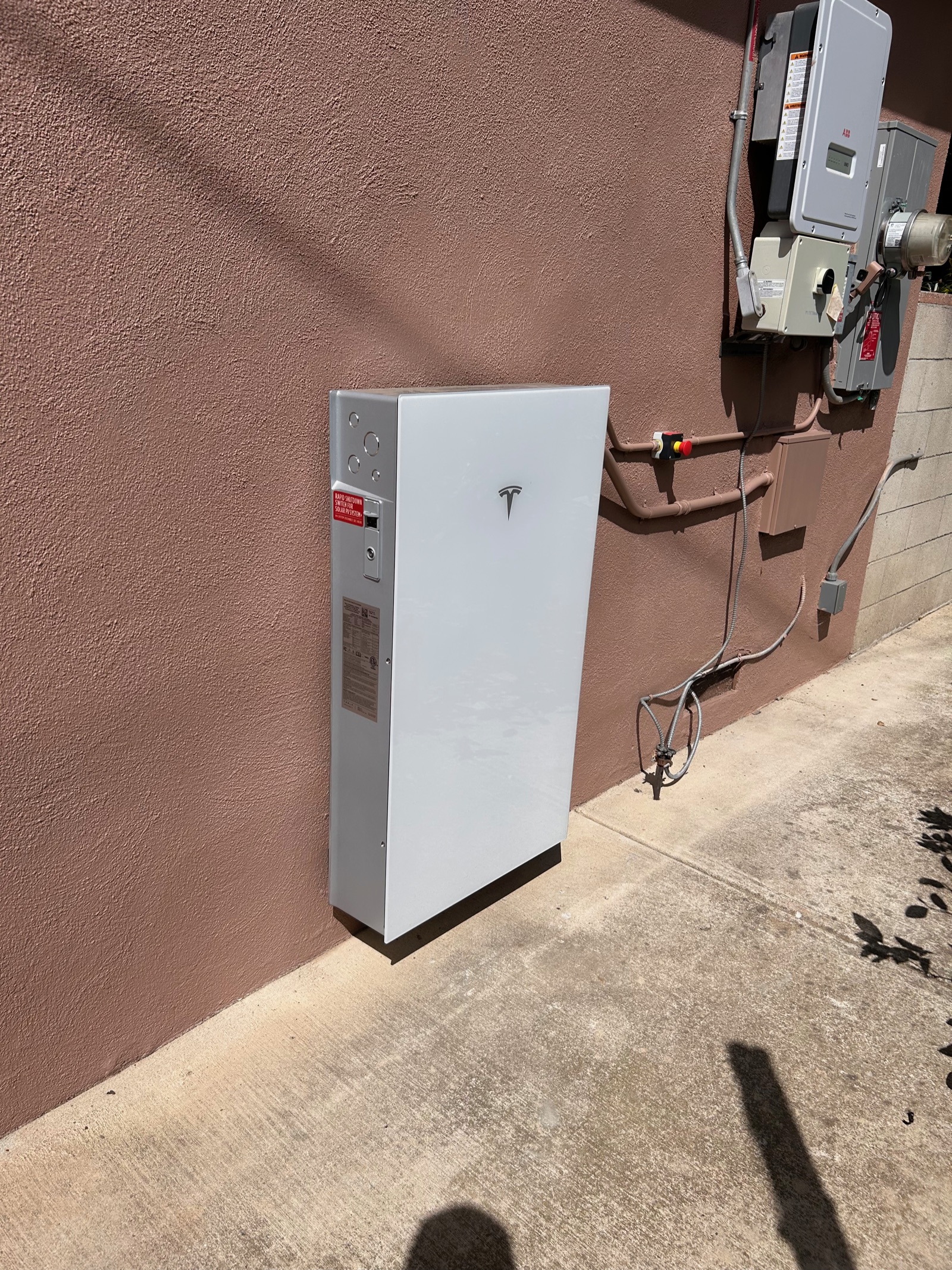 White backup system cabinet and inverter mounted on an exterior stucco wall with clean conduit runs